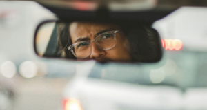 A person driving and looking in the rearview mirror, possibly at an aggressive driver
