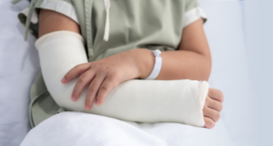 A person in a hospital gown cradles their arm, which is wrapped in a cast